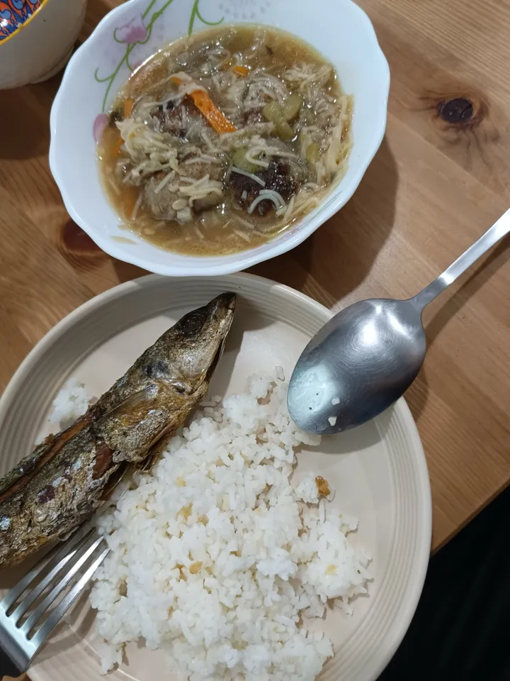 A home dinner on a table: fried fish, a plate of rice, and a bowl of soup.